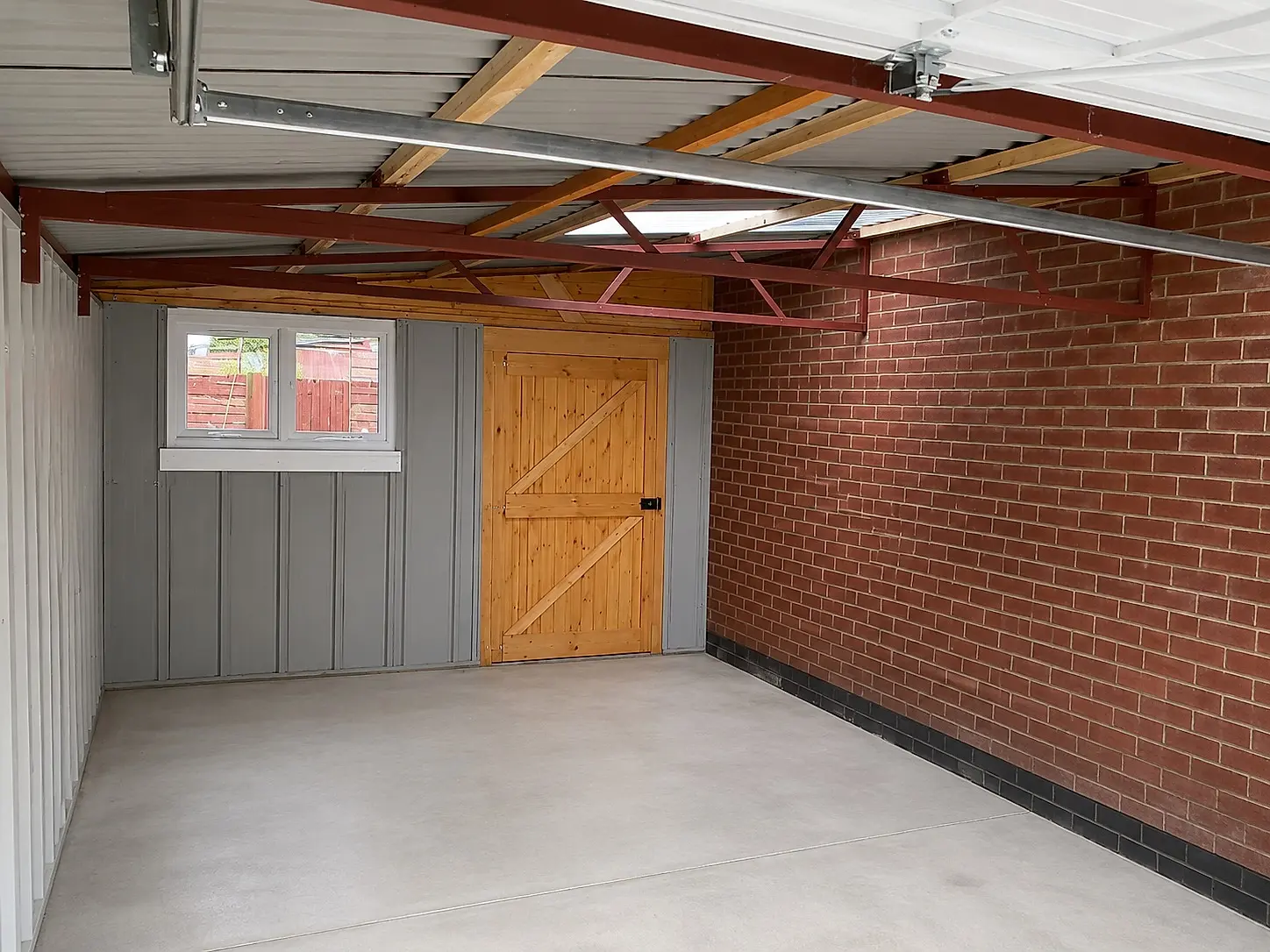 Inside a lean-to concrete garage showing the mono-pitch roof, timber personnel door and brick party wall