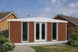 Garden room with red brick-effect panels and a hip roof in a suburban rear garden