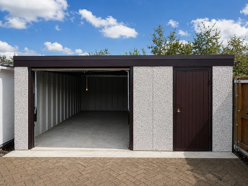 Single pent roof concrete garage with the up-and-over door open, showing the interior, alongside a brown personnel door