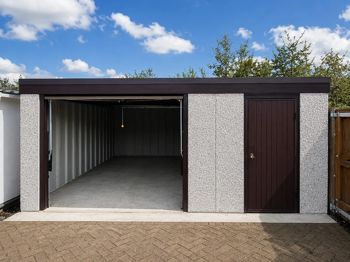 Single pent roof concrete garage with the up-and-over door open, showing the interior, alongside a brown personnel door