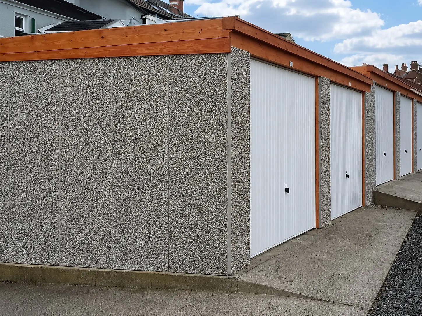 Concrete battery garages with white up-and-over doors and a red cedar timber fascia