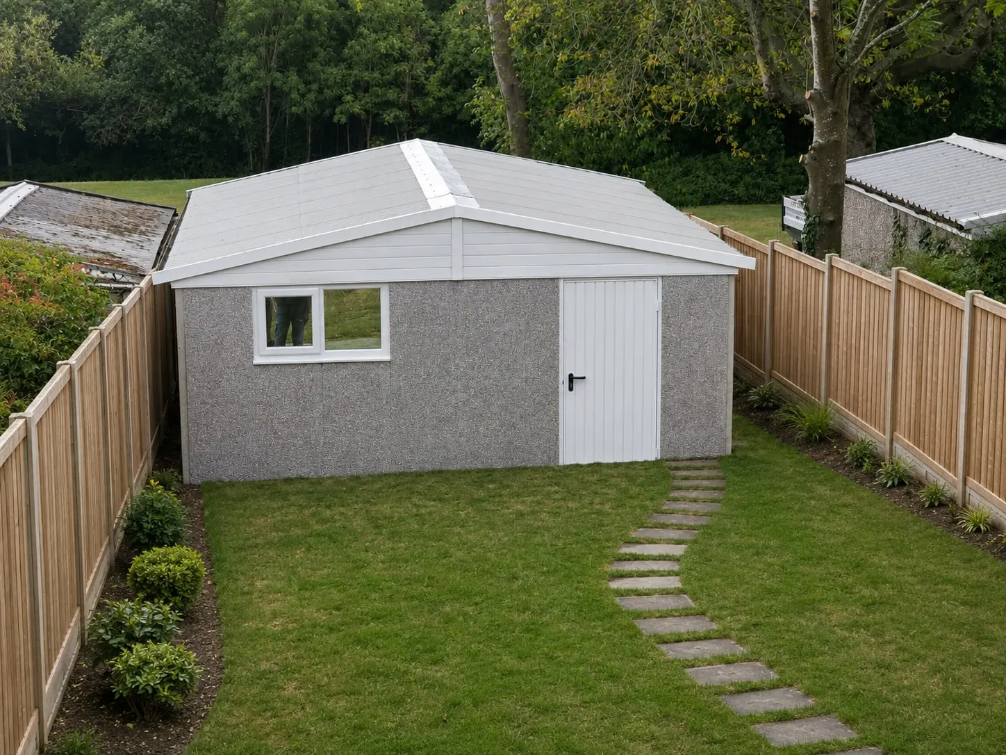 Concrete shed with an apex roof, window and personnel door on a lawn