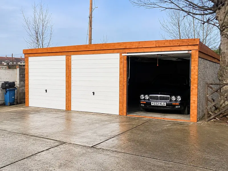 Concrete battery garage with a car parked inside an open bay, alongside two white up-and-over doors