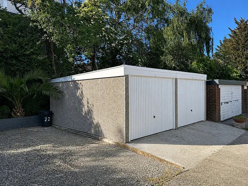 Double pent roof concrete garage with two white up-and-over doors and a pebbledash finish