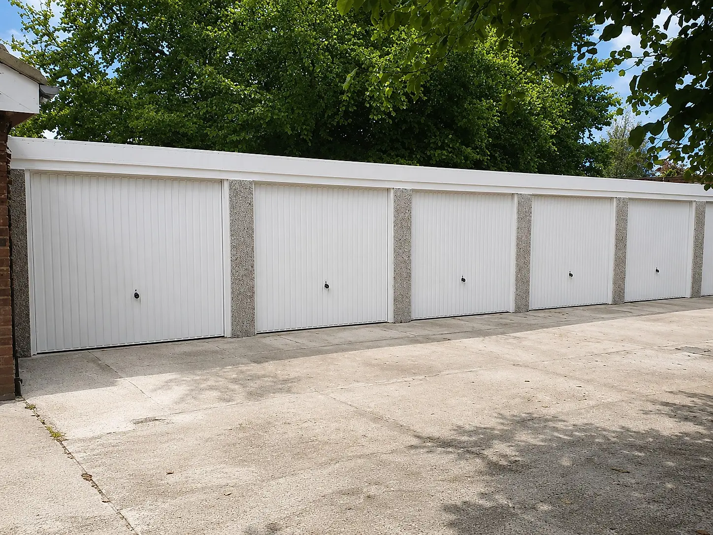 Row of concrete battery garages with white up-and-over doors and pebbledash pillars