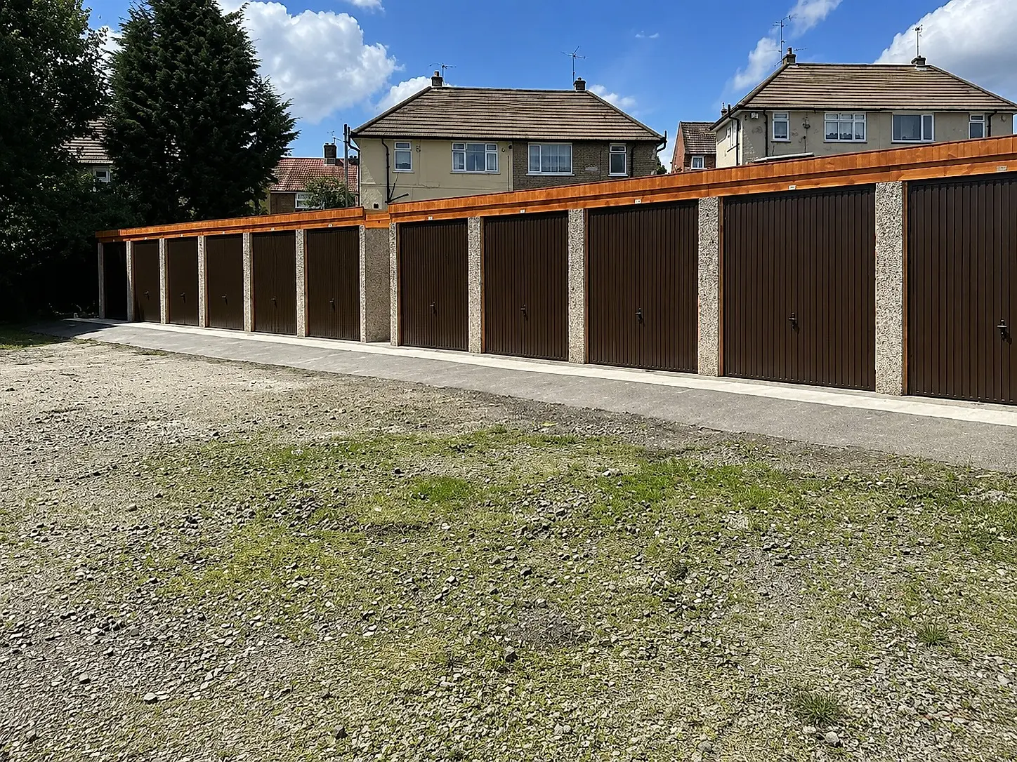 Row of concrete battery garages with brown up-and-over doors and a red cedar fascia on a housing estate