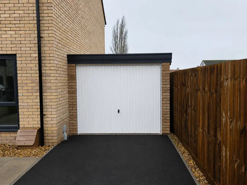 Lean-to concrete garage with a white up-and-over door on a tarmac driveway