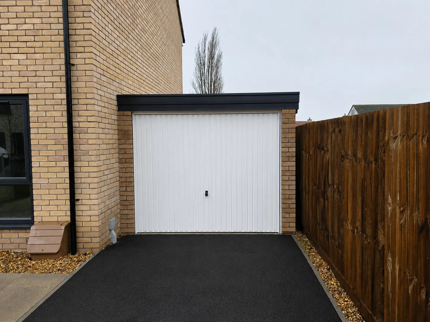 Lean-to concrete garage with a white up-and-over door on a tarmac driveway