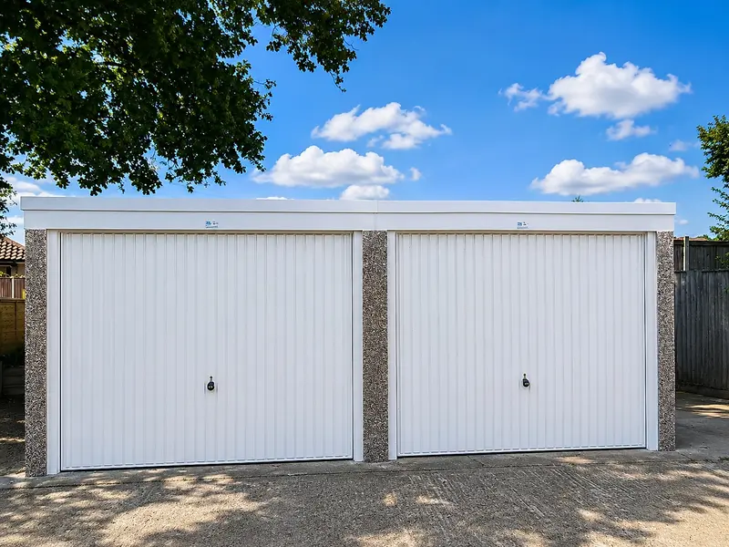 Double pent roof concrete garage with two white up & over doors and pebbledash pillars, front view on a concrete drive
