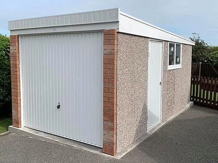 Single pent roof concrete garage, side view showing the sloping roof and pebbledash finish with potted plants
