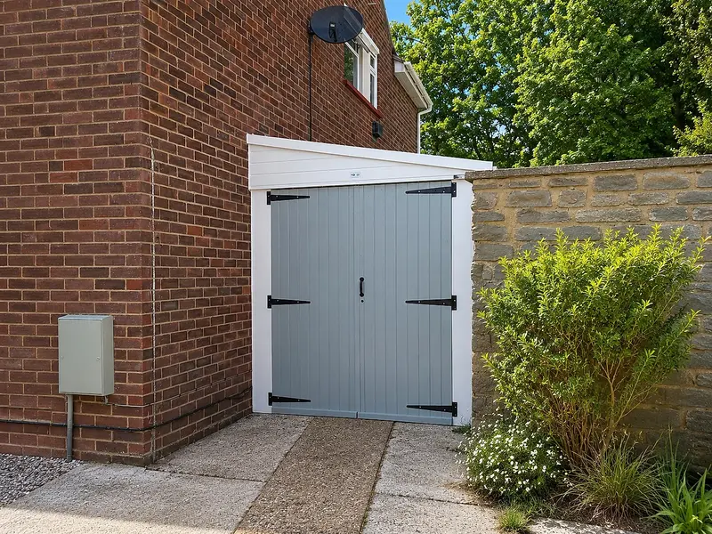 Lean-to concrete garage with grey side-hinged timber doors against a brick house