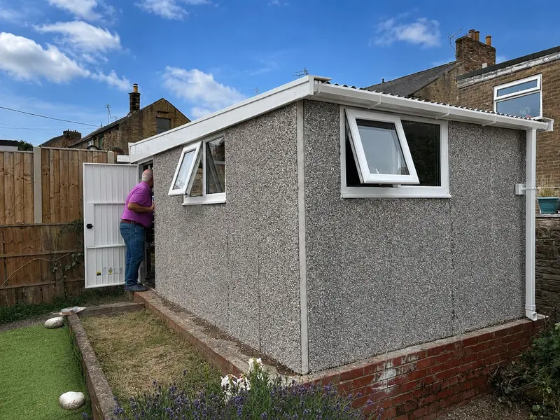 Pent roof concrete garage with a pebbledash finish and window in a landscaped garden