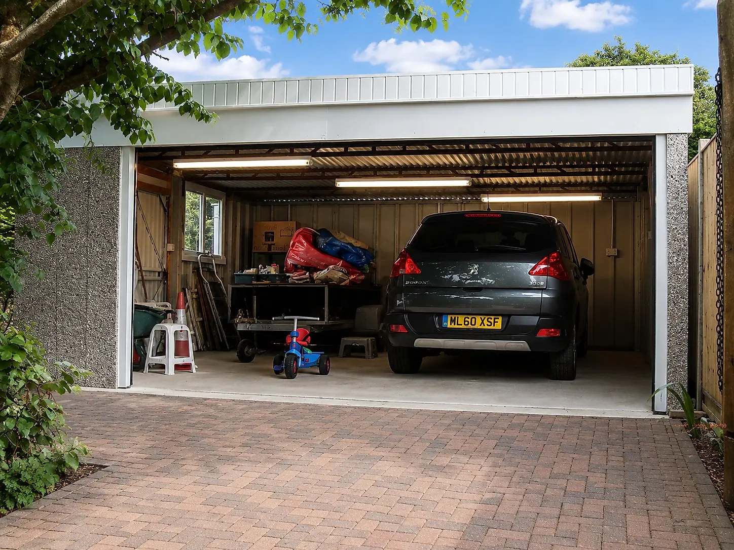 Extra-height concrete garage with the door open, a car and workshop storage inside showing the tall interior