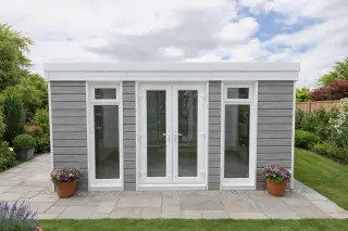 Garden room with grey composite cladding, white door frames, French doors, and a flat pent roof in a landscaped garden