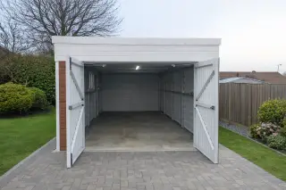 Single garage with white composite cladding and double swing doors fully open, showing interior lighting